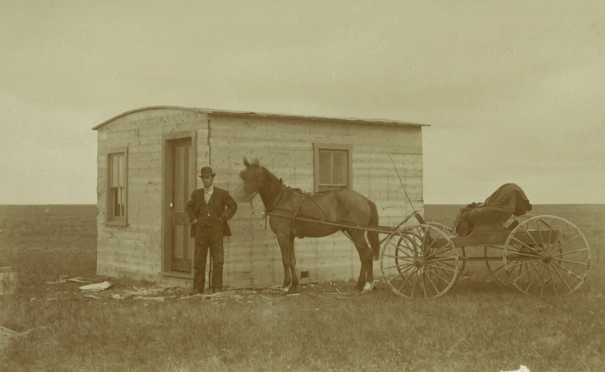 Man with horse and buggy beside a small shack on the prairie